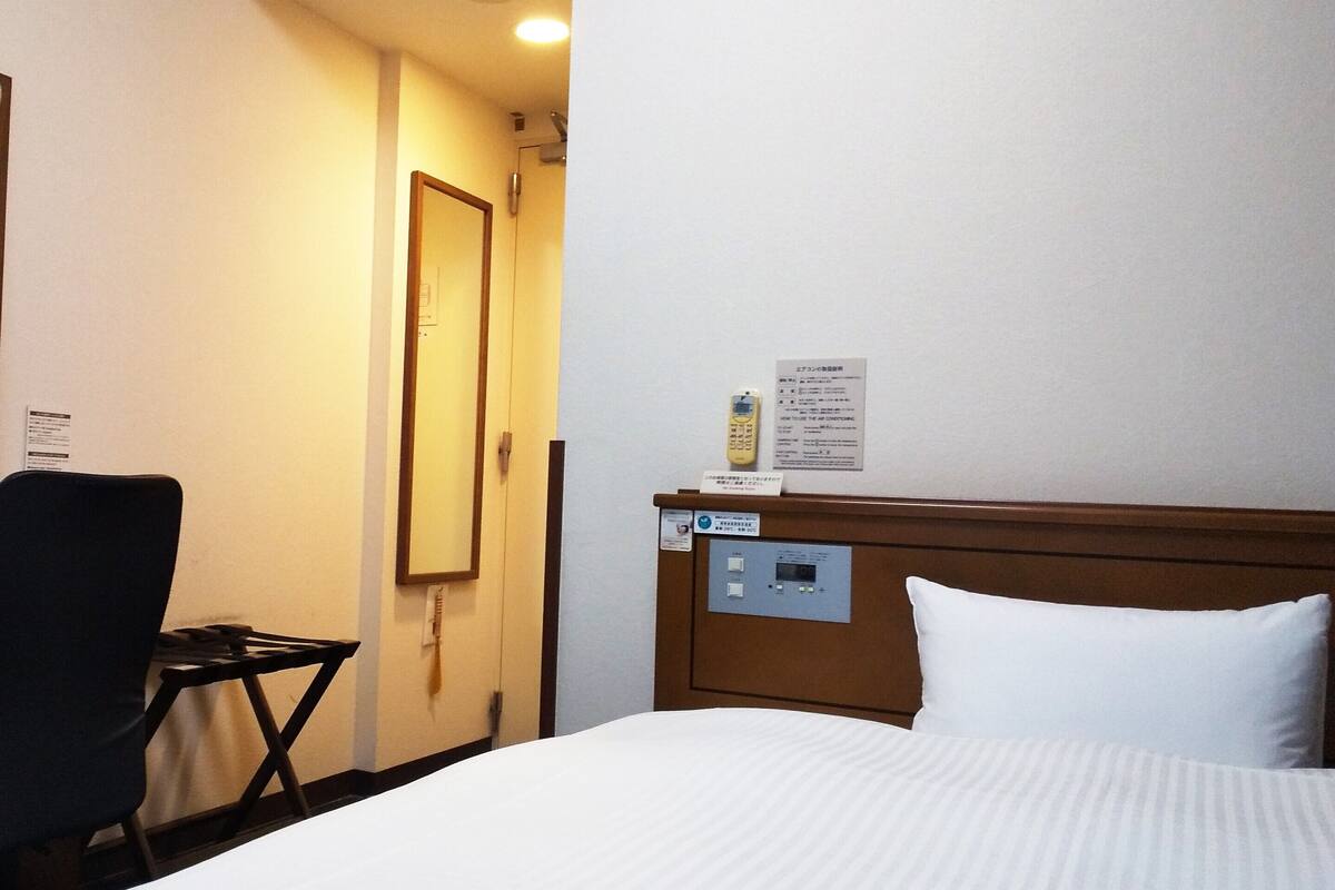 A hotel room with a bed, a chair, a desk, and a phone.