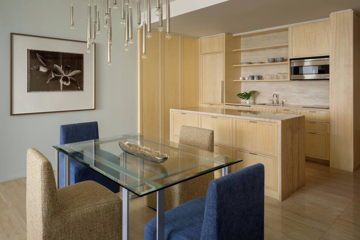 Una cocina moderna con armarios de madera, una mesa de comedor de vidrio y una lámpara colgante.