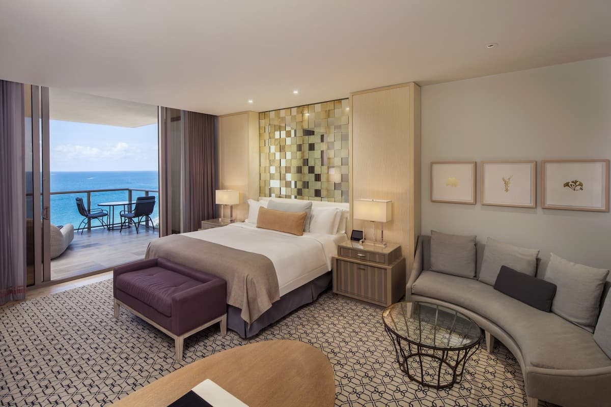 Una habitación de hotel con cama, sofá, mesa de centro de vidrio y vista al océano.