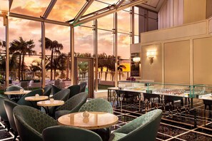 A restaurant with round tables and green upholstered chairs, large windows, and a view of palm trees. - The St. Regis Bal Harbour Resort (Bal Harbour)