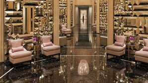 Un hall d’entrée luxueux, agrémenté d’un grand lustre, de murs recouverts de miroirs et de fauteuils confortables.