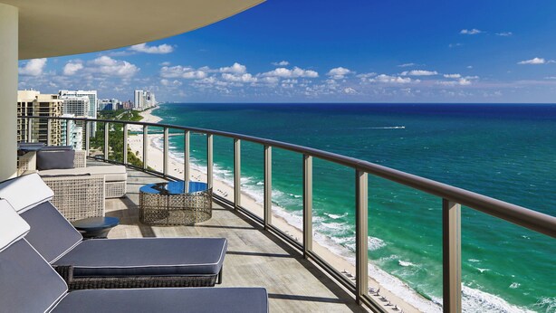 Un balcon avec des sièges d’extérieur, une vue sur l’océan et une plage.