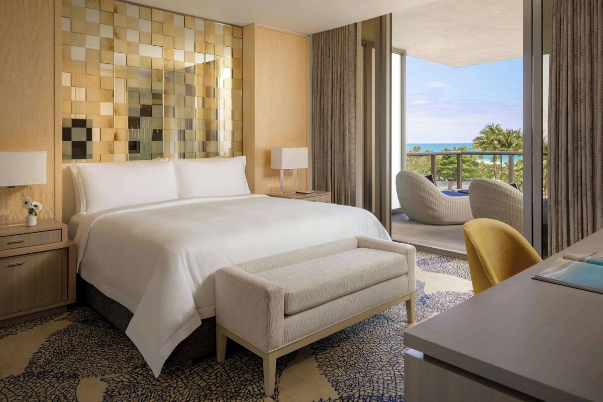 Habitación de hotel con una cama grande, un escritorio, una silla, un balcón con vista al océano y un adornado en la pared.
