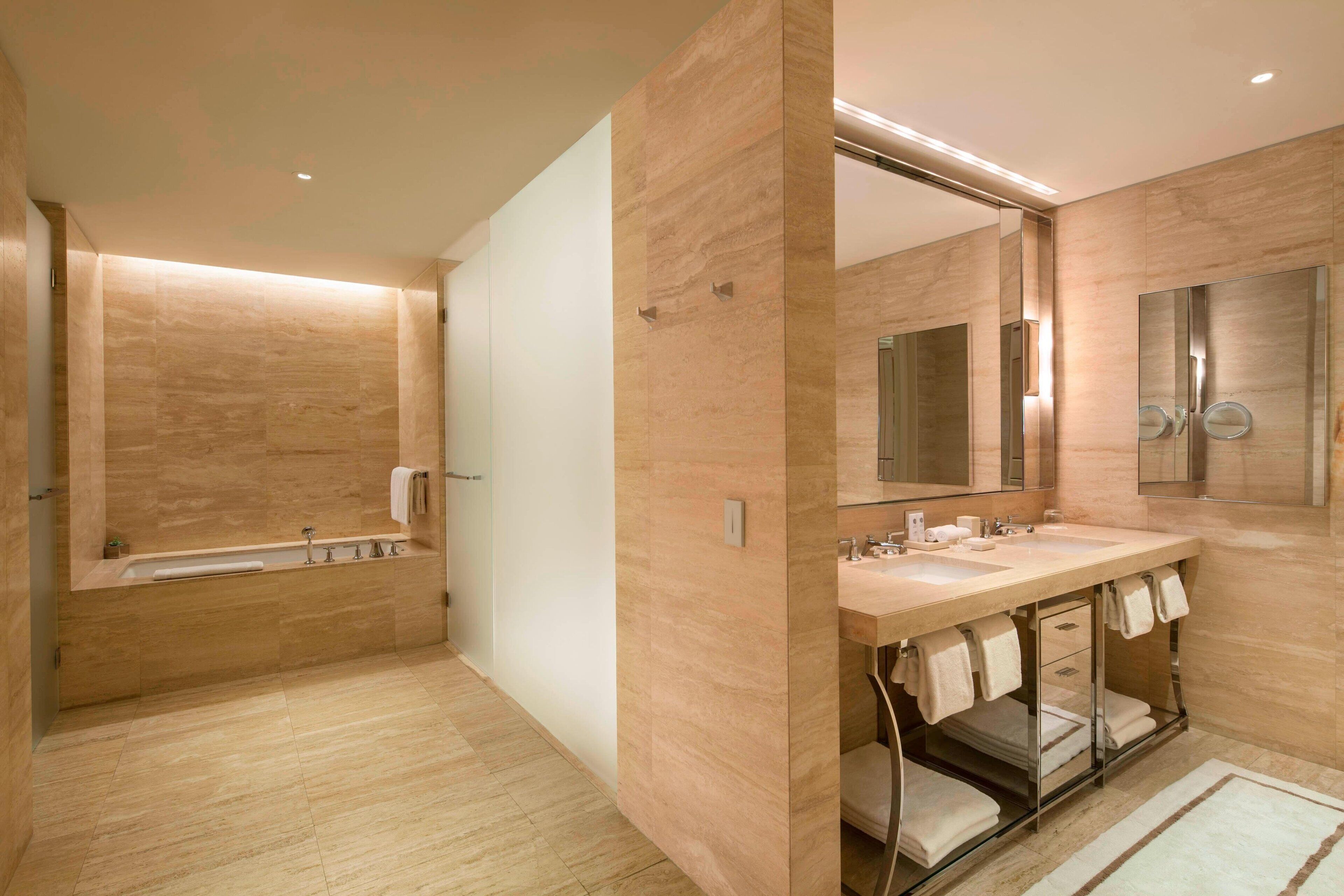 Un baño moderno con un espejo grande, dos lavamanos, una bañera y una ducha a ras de suelo.