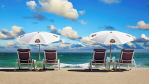 Quatre chaises de plage, placées sous des parasols blancs ornés d’un logo, sont disposées face à l’océan.
