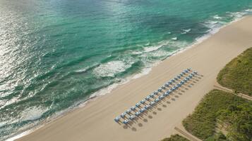 Vue aérienne d’une plage bordée d’une rangée de parasols et de chaises longues.