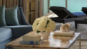 Un salon moderne avec vue sur l’océan, comprenant un canapé, une table basse avec des livres et un vase de fleurs, ainsi qu’une lampe.