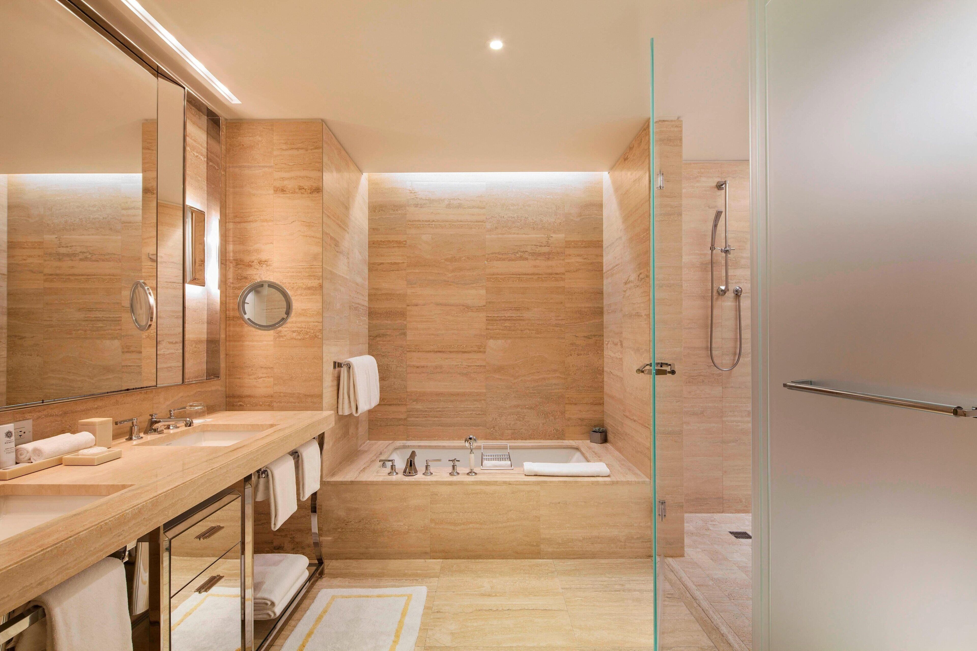 Un baño moderno con tocador doble, un espejo grande, una bañera y una ducha con mampara de vidrio.