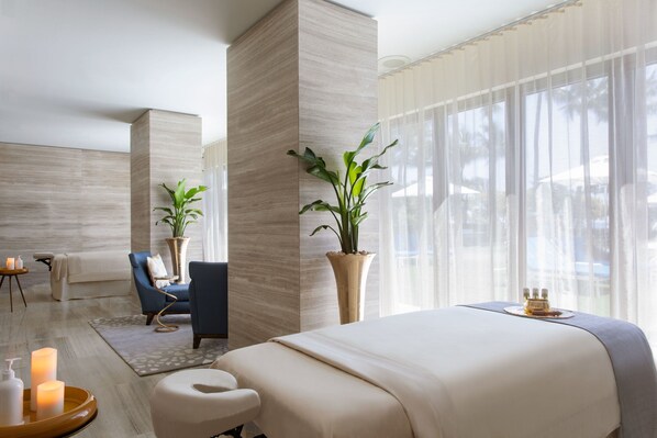 A modern hotel room with a large bed, a sitting area with a chair and a small table, a large window with sheer curtains, and two potted plants. - The St. Regis Bal Harbour Resort (Bal Harbour)