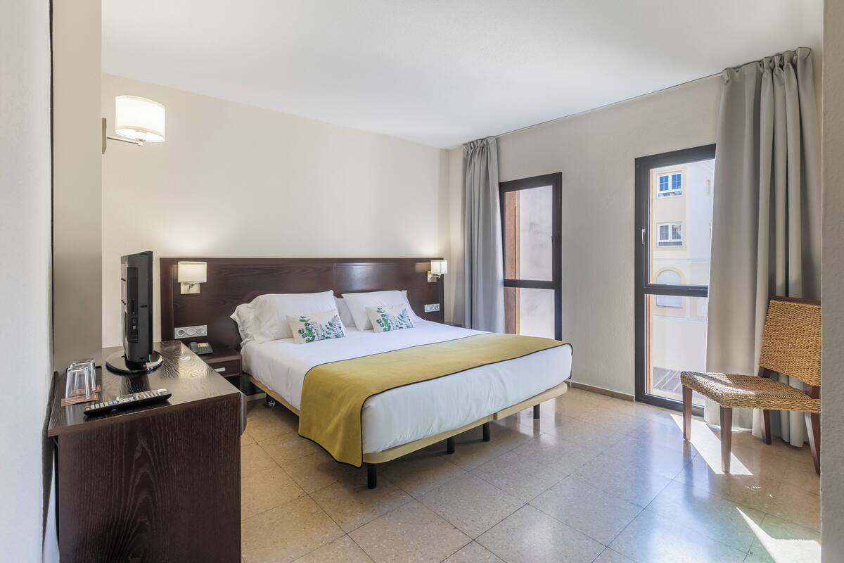 Una habitación de hotel con cama, mesita de noche, lámpara y una silla.