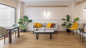 Un salón moderno con sofá, mesa de centro y sillones. Hay plantas en macetas y una lámpara colgante.