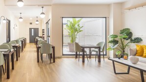 Un comedor moderno con mesas y sillas de madera, ventanas amplias con plantas, y un interior luminoso.