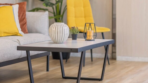 Una sala de estar moderna con un sofá, una mesa de centro y una silla amarilla. Se observa una escalera al fondo.