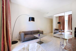 Una sala moderna con un sofá gris, una mesita con una planta en maceta, una lámpara de pie y un espejo grande que refleja la habitación.