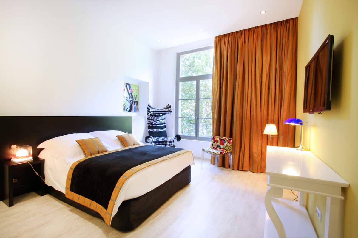 Une chambre moderne avec un grand lit, une table de chevet avec une lampe, une chaise et un téléviseur fixé au mur.