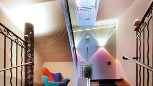 Una escalera con alfombra azul, una silla colorida y una planta.