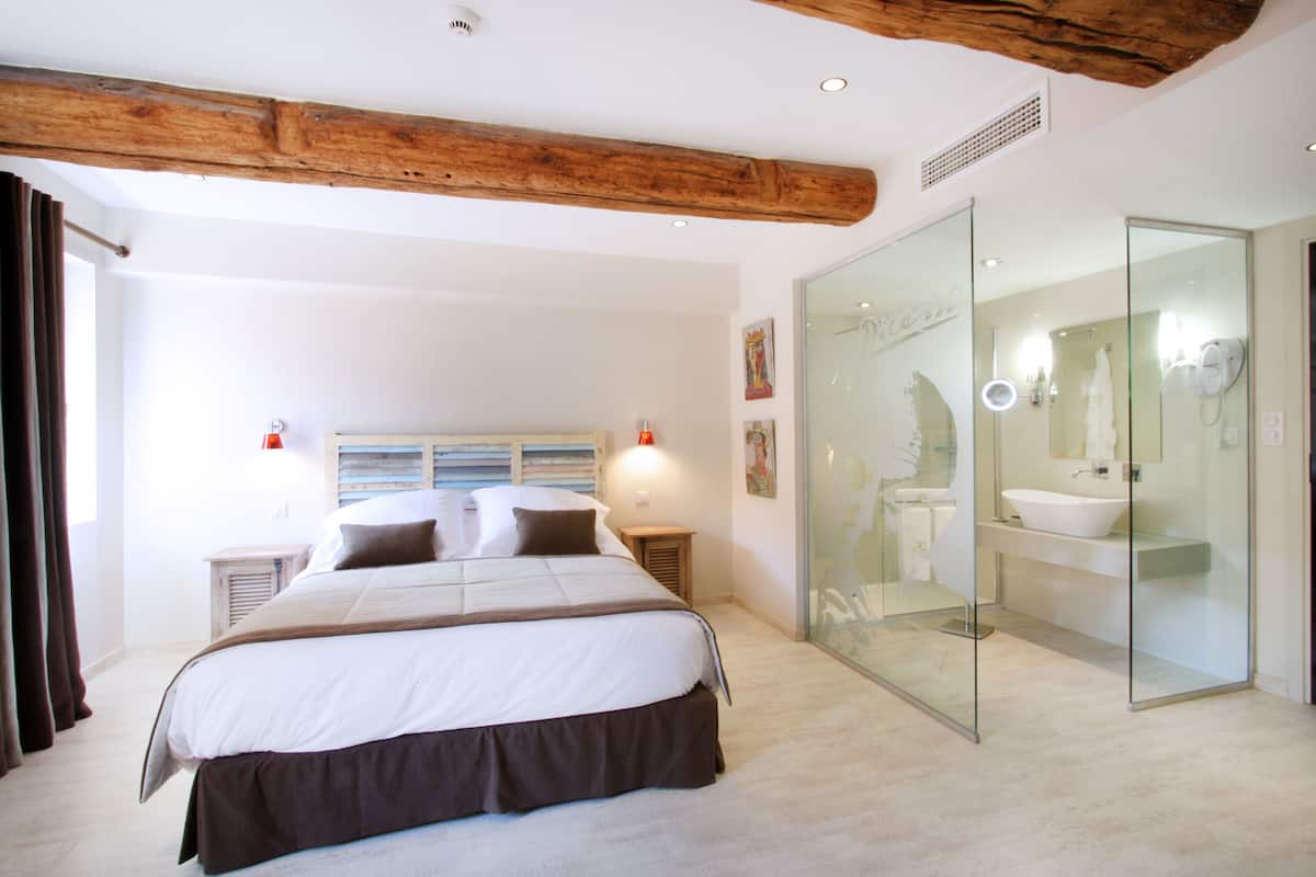 Une chambre moderne avec un grand lit, une douche en verre et une poutre en bois au plafond.