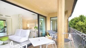 Un balcón moderno con mobiliario blanco, que incluye un sofá y sillones, y una mesita.