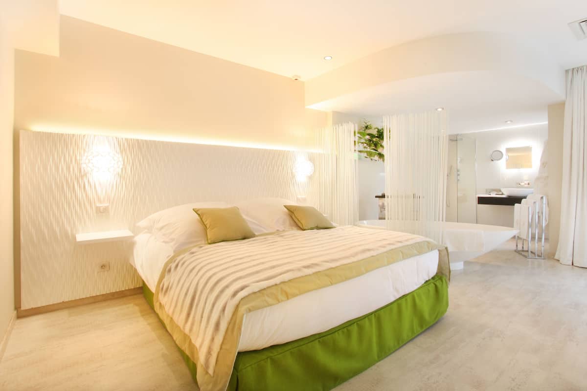 Une chambre moderne avec un grand lit, des tables de chevet, un miroir et une salle de bain équipée d’une douche et d’un lavabo.