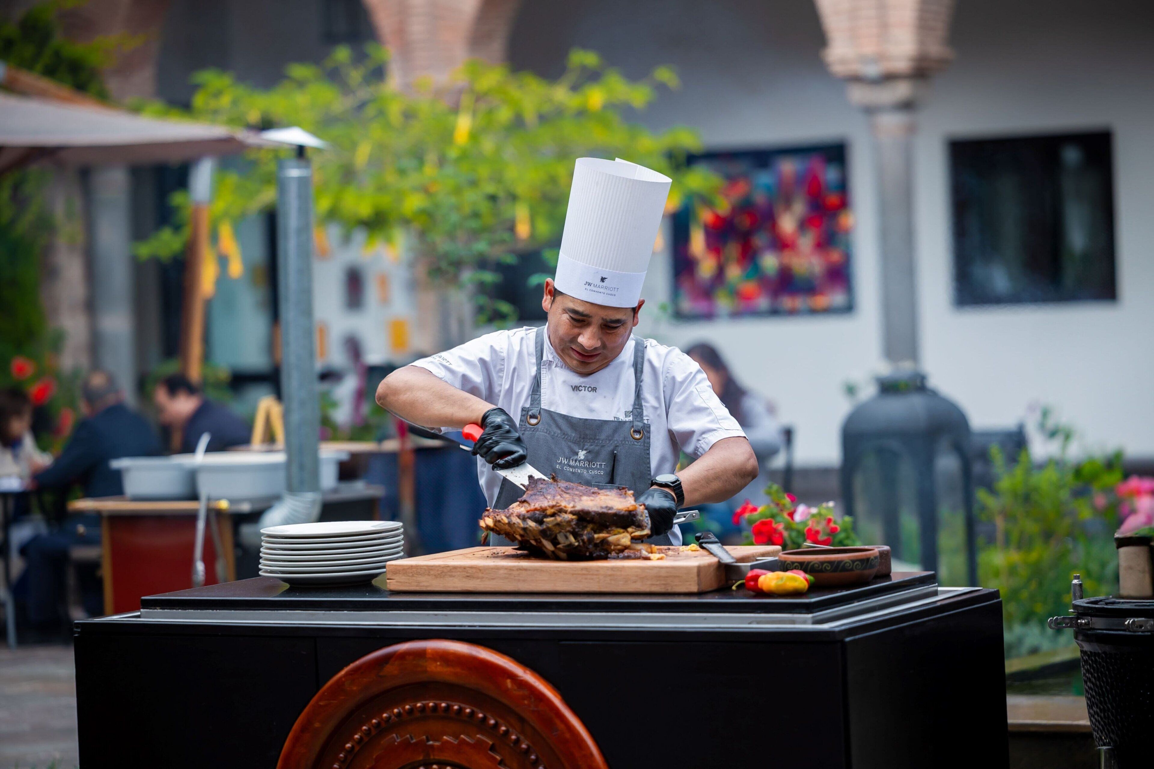 Un chef preparando comida al aire libre, con una parrilla y platos sobre una mesa.