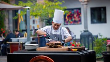 Un chef preparando comida al aire libre, con una parrilla y platos sobre una mesa.