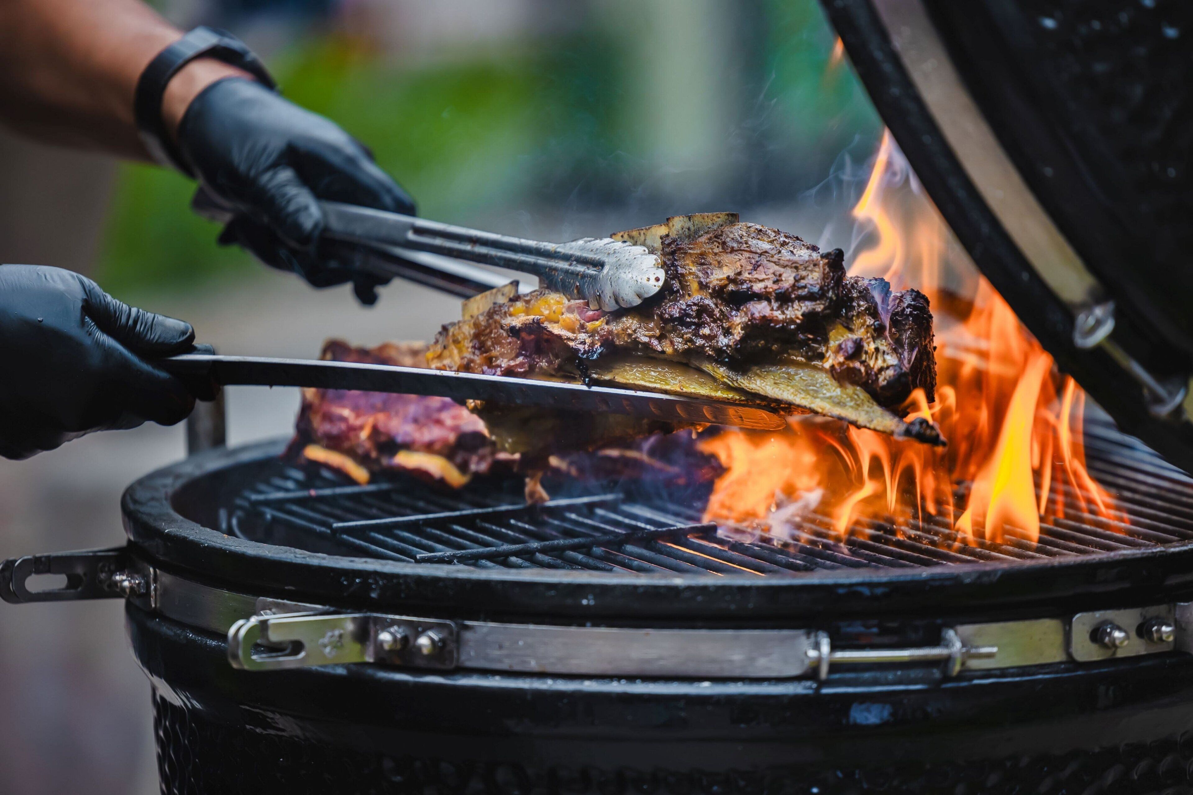 A person grilling meat on an outdoor grill with visible flames.