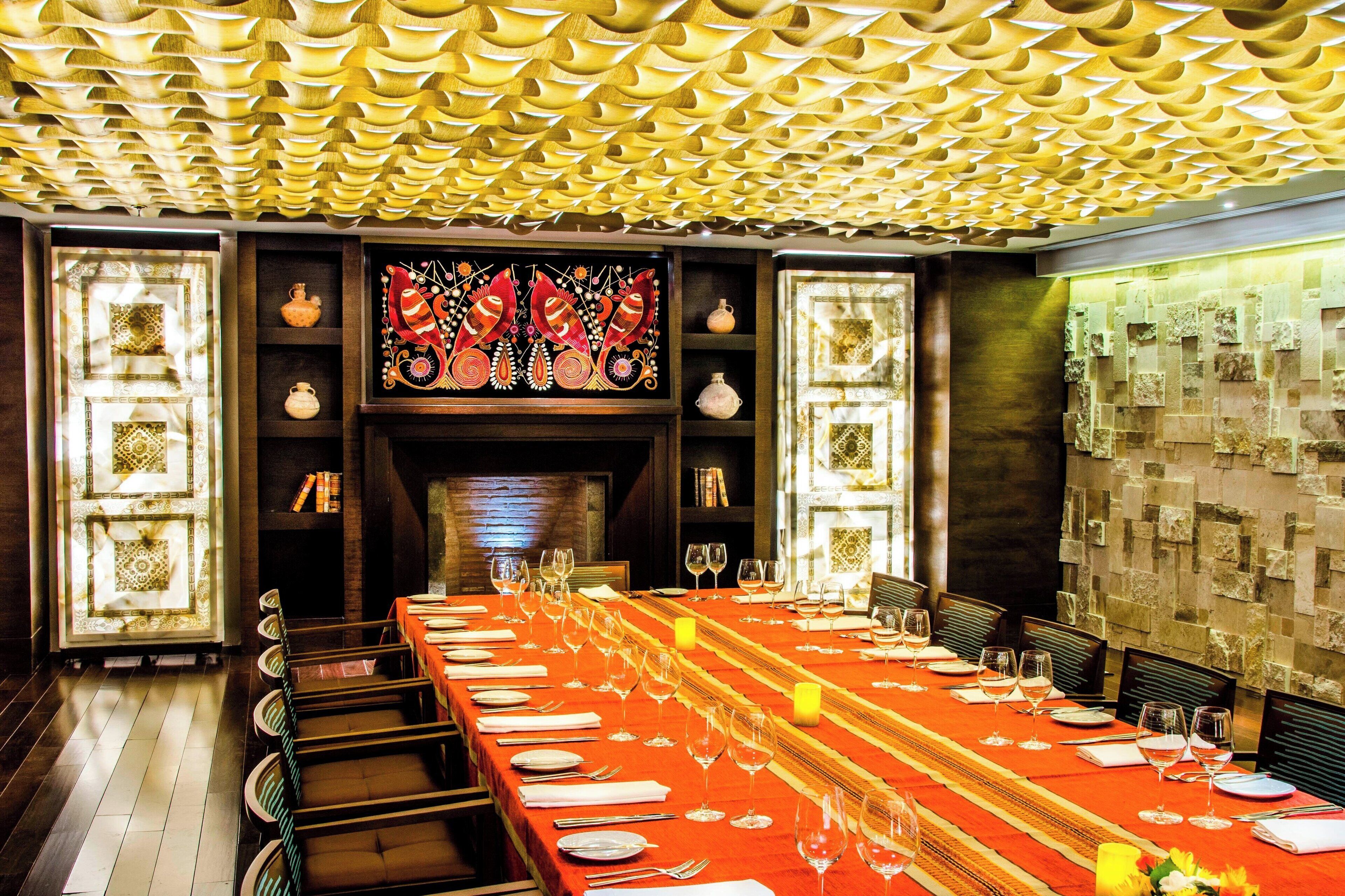 Un comedor con una mesa larga dispuesta para una comida, rodeada de sillas, con un techo estampado y paneles decorativos en las paredes.