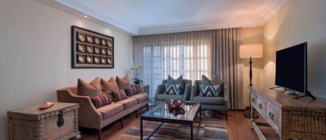 Uma sala de estar com sofá, mesa de centro, TV e um detalhe decorativo na parede.