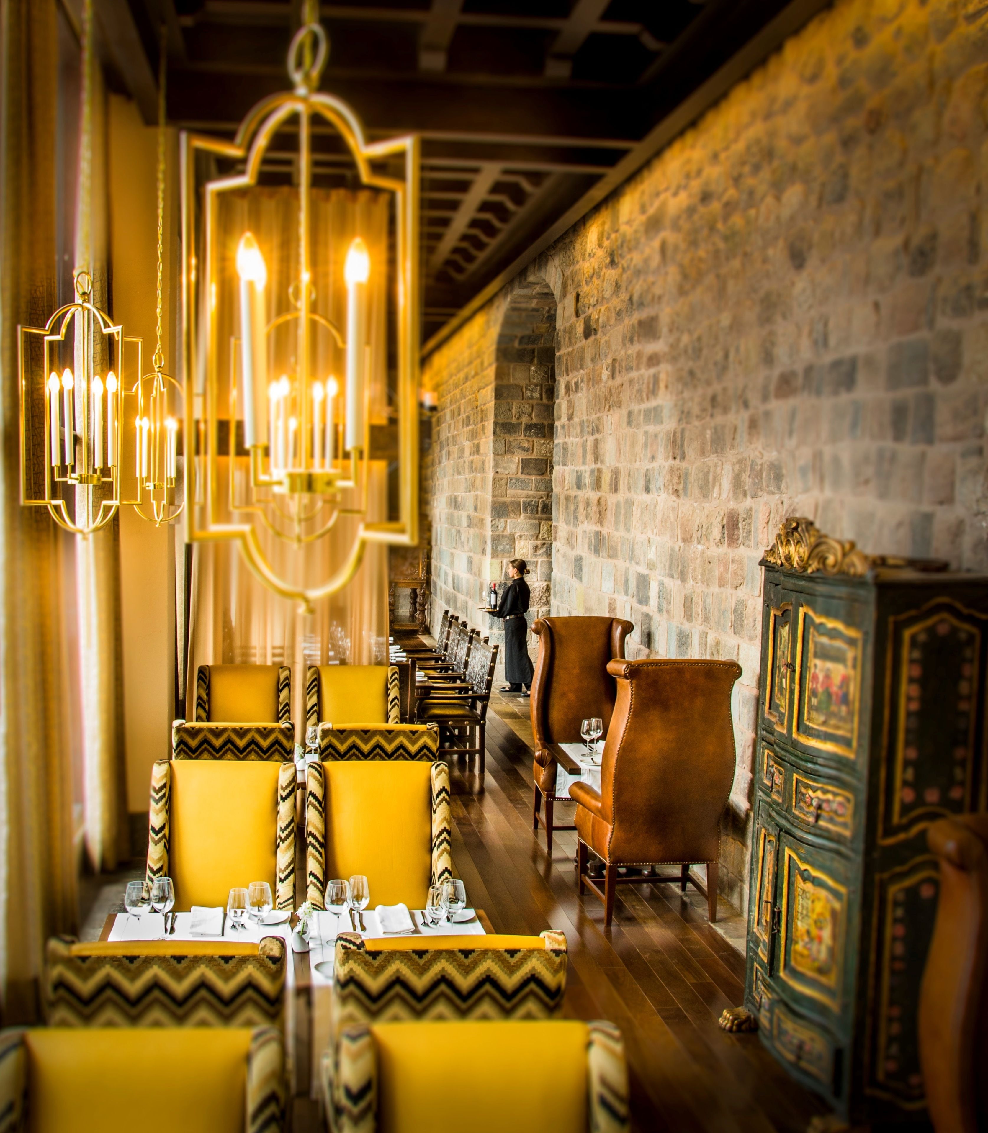 A restaurant with a stone wall, wooden tables, and yellow chairs.