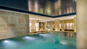 A modern indoor swimming pool with a clear pool, stone walls, and a seating area with cushions and a vase of flowers. - JW Marriott El Convento Cusco (Cusco)