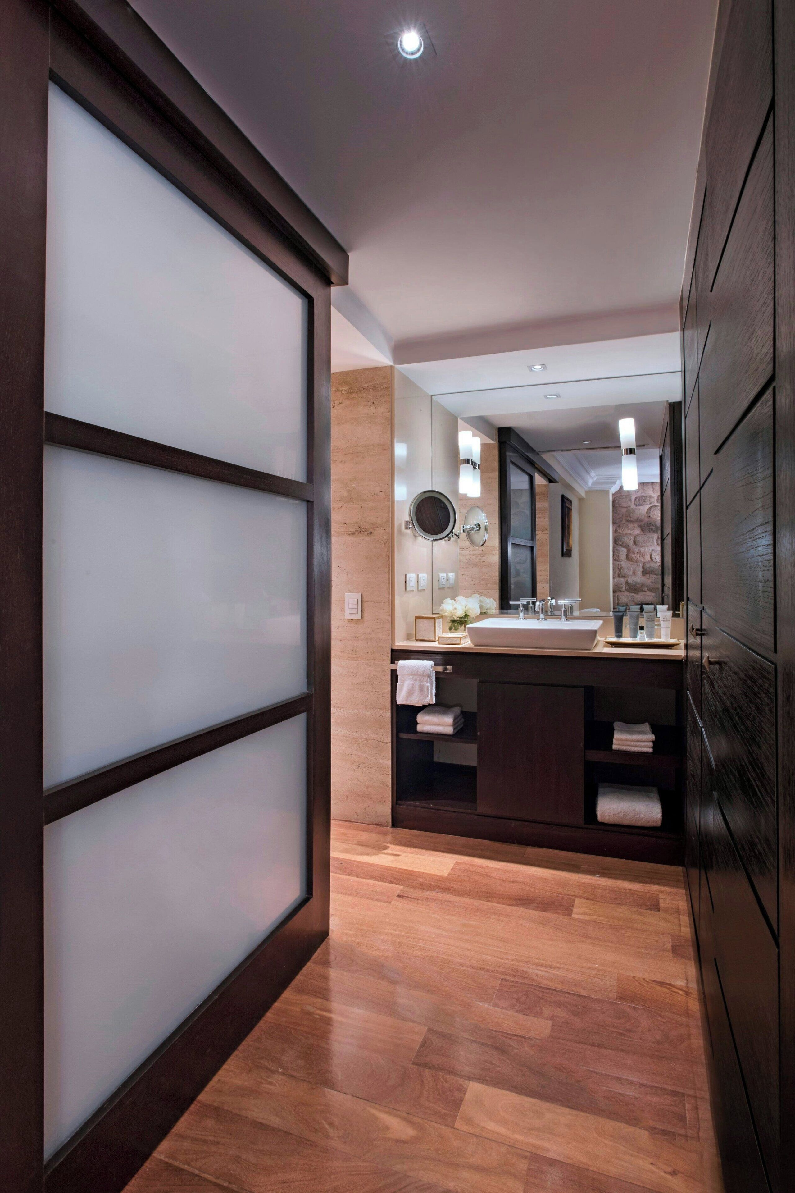 Un baño moderno con un espejo grande, tocador de madera y piso de baldosas.