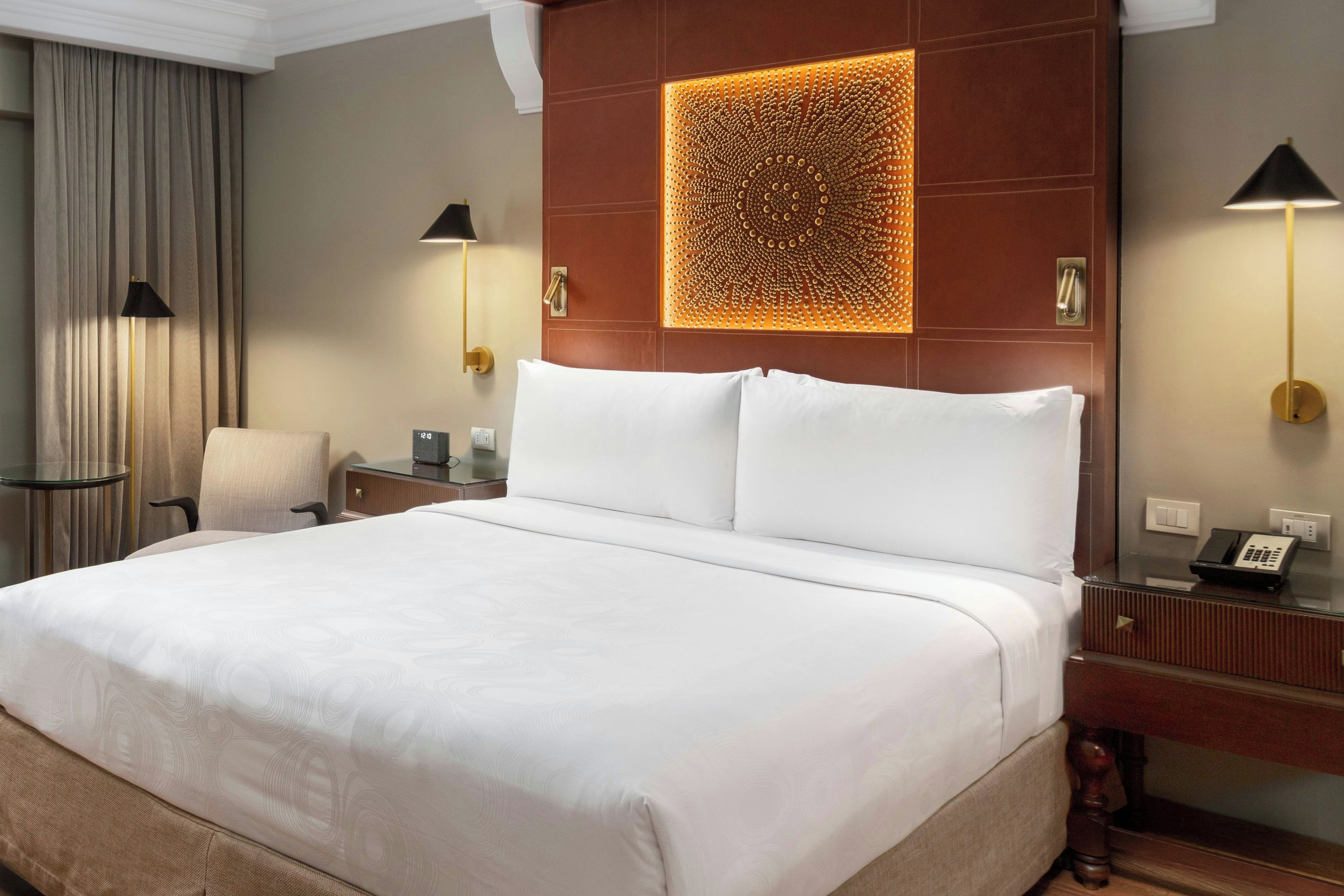 Una habitación de hotel con una cama grande, un escritorio con teléfono, una silla y una lámpara.