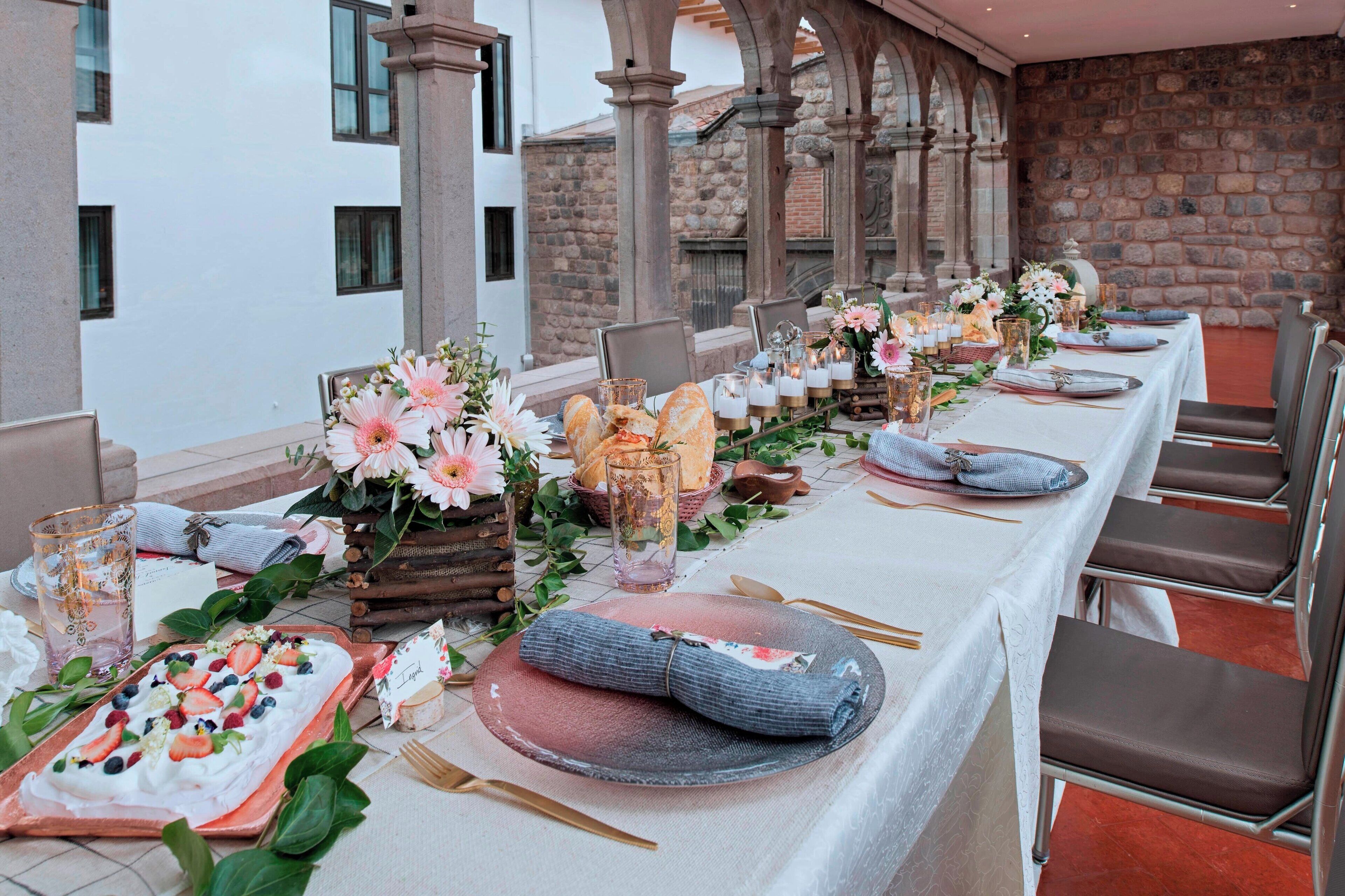 A long dining table set with floral centerpieces, bread baskets, and a dessert tray.