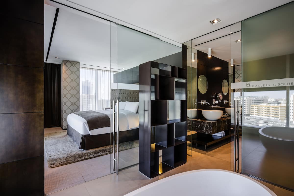 Ein modernes Schlafzimmer mit einem großen Bett, einem Badezimmer mit Glaswand und Badewanne sowie Blick auf die Stadt.