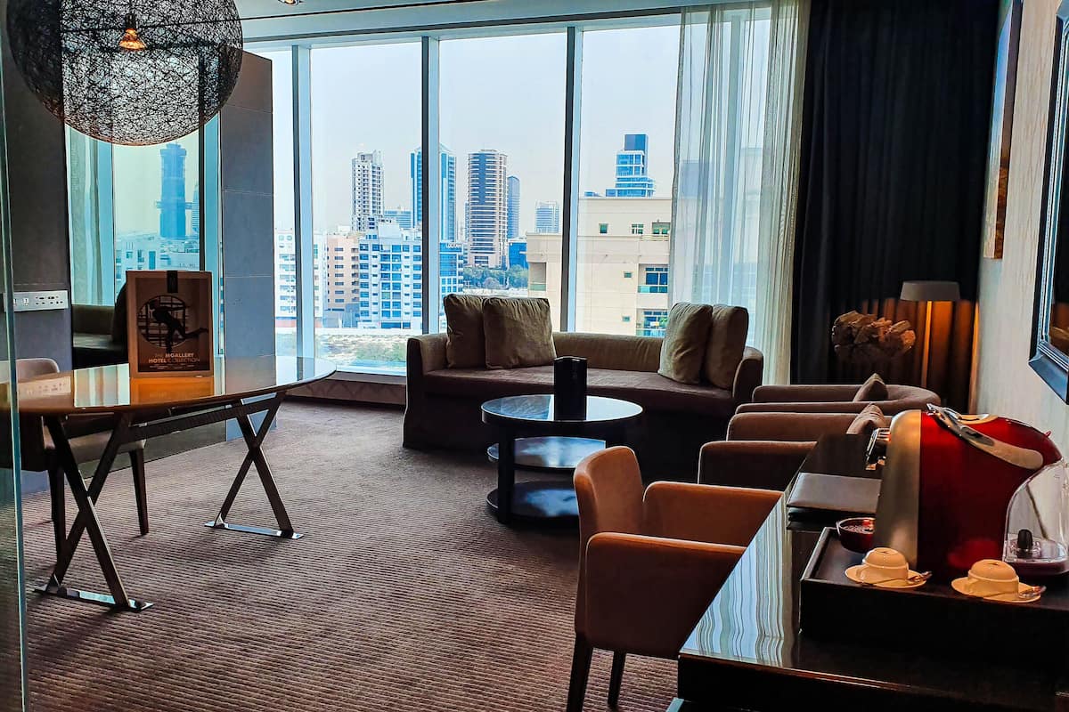 Ein modernes Hotelzimmer mit großem Fenster und Blick auf die Stadt, inklusive Sofa, Couchtisch und Essbereich mit einer Teekanne und einer Teetasse.