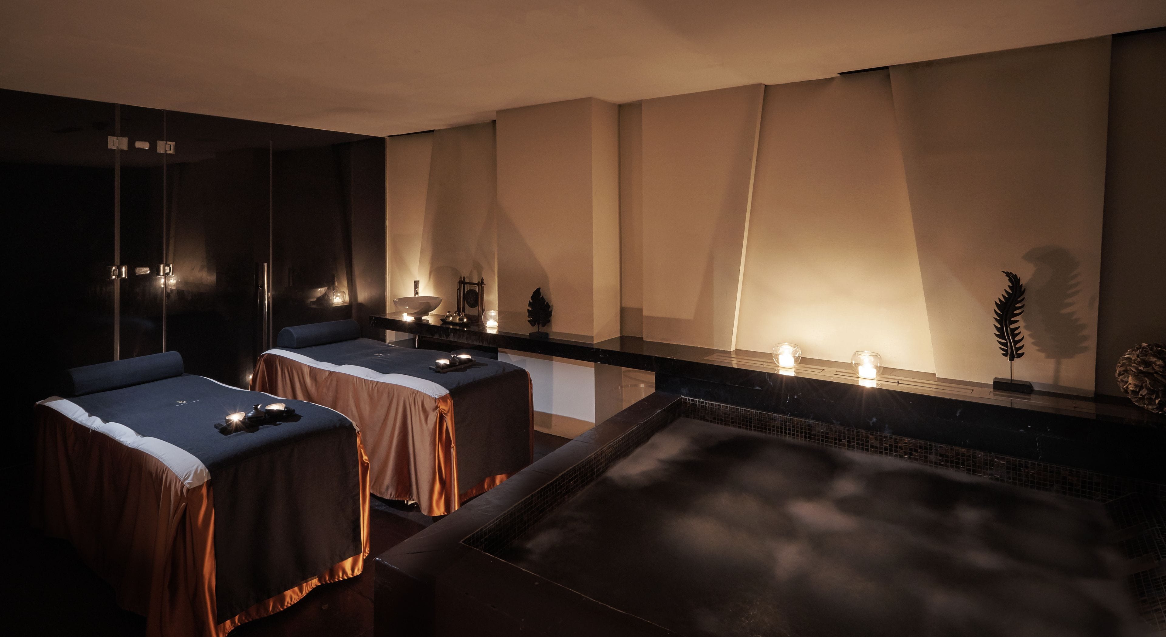 A spa room with two massage tables, a large heated tub, and a wall-mounted massage table.