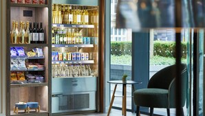 A modern bar area with shelves of bottled beverages, snacks, and a seating area with a chair and a small table. - Residence Inn by Marriott Edinburgh (Edinburgh)