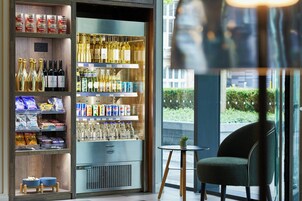 A modern bar area with shelves of bottled beverages, snacks, and a seating area with a chair and a small table.