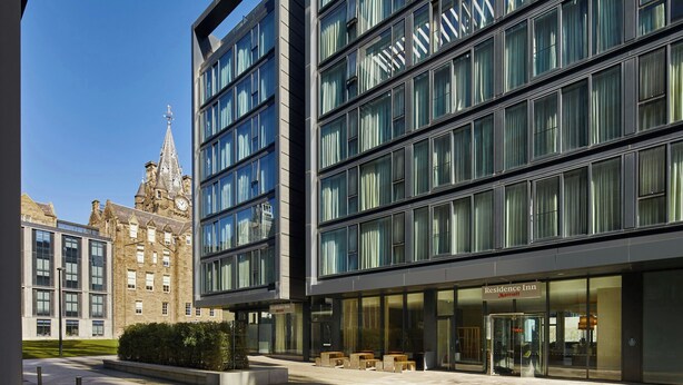 A modern hotel with a glass facade, a traditional building in the background, and outdoor seating. - Residence Inn by Marriott Edinburgh (Edinburgh)