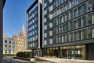 A modern hotel with a glass facade, a traditional building in the background, and outdoor seating.