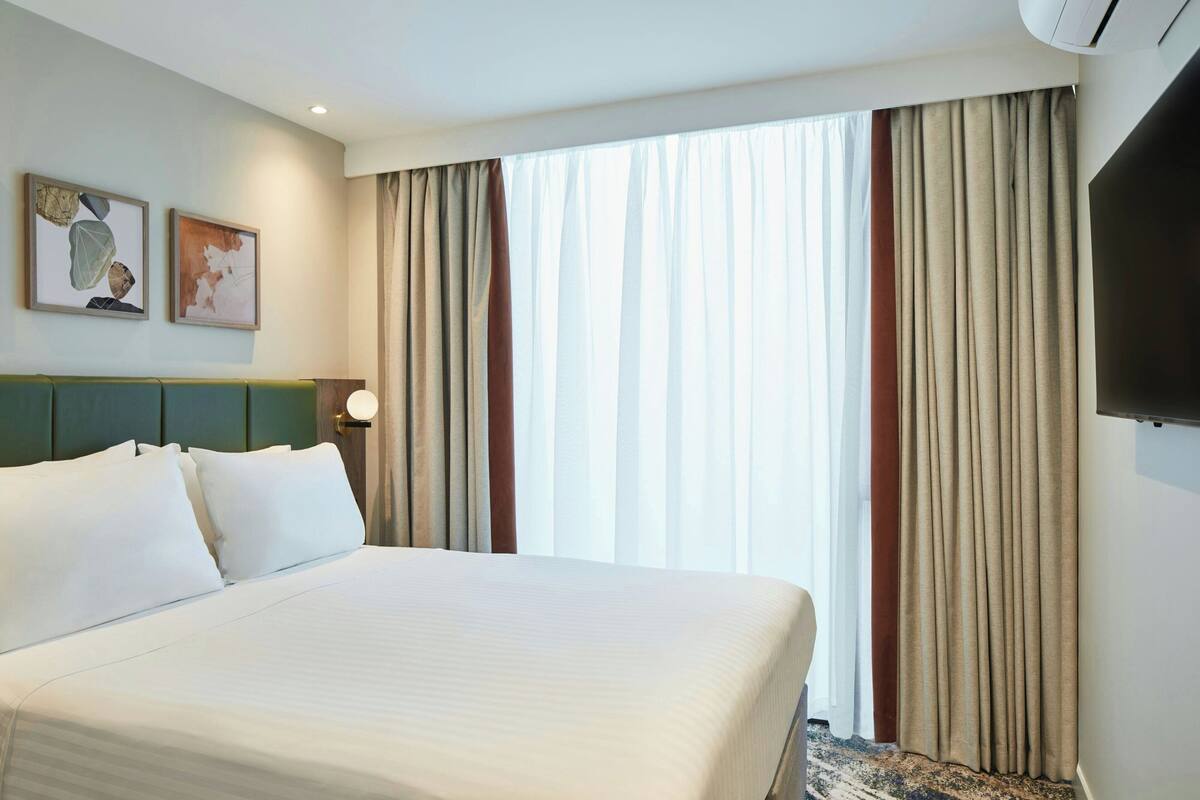 A hotel room with a large bed, a flat-screen TV, and a window with curtains.