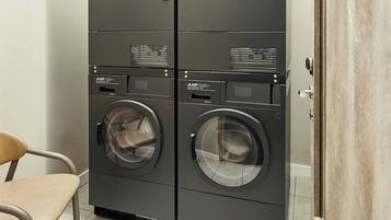 A laundry room with two front-loading washing machines and a chair.