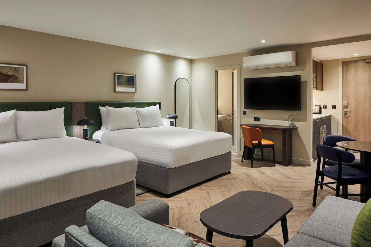 A hotel room with two beds, a desk, a TV, and a seating area.