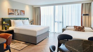 A hotel room with a large bed, a desk with a chair, a small table, and a view of the city through large windows. - Residence Inn by Marriott Edinburgh (Edinburgh)