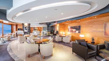 A modern hotel lobby with a curved ceiling, seating areas, a bar, and a large window offering a view.