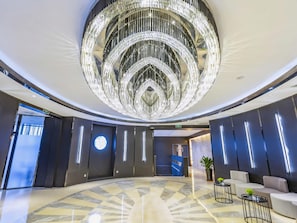 A lobby with a large circular chandelier, a marble floor, and modern seating areas.