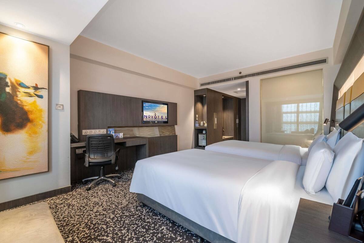 Een hotelkamer met een bed, een bureau, een televisie en een schilderij aan de muur.