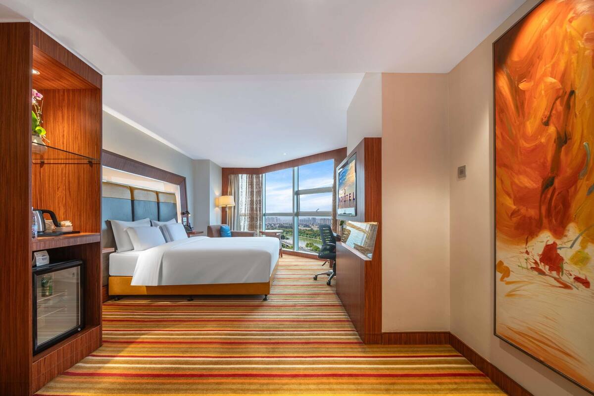 Een hotelkamer met een groot bed, een bureau, een stoel, een televisie en uitzicht op de stad.