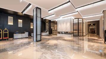 Een moderne hotellobby met een receptiebalie, een grote marmeren kolom en een trap naar de verdiepingen.