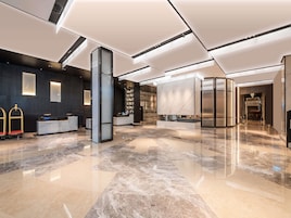 A modern hotel lobby with a reception desk, a large marble column, and a staircase leading to the upper floors.
